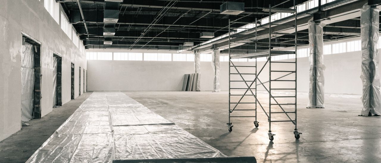 Open commercial interior with suspended work lighting and protective floor covering during ceiling work