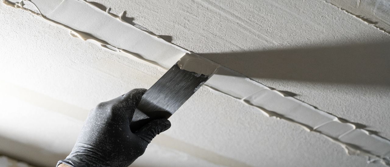 Drywall compound being floated over a repaired ceiling seam with a wide taping knife