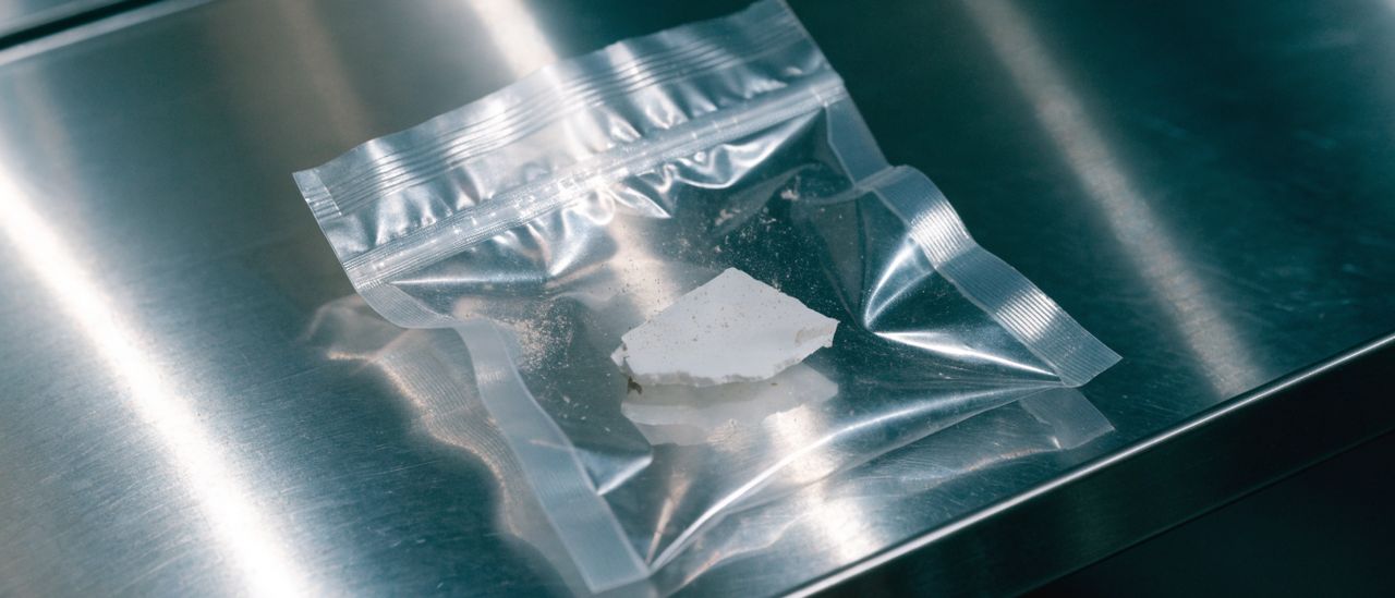 Gloved hand collecting a small sample of ceiling texture into a labeled specimen bag